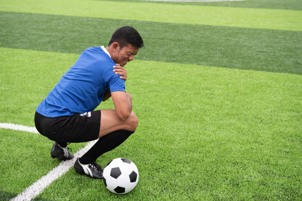 Mavi bir gömlek, siyah pantolon içinde çim yarış sırasında yaralı giyen futbolcu. - Fotoğraf, Görsel