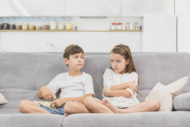 Cute children eating popcorn while watching TV at home. a little girl is offended because the brother does not give her a popcorn - Foto, afbeelding