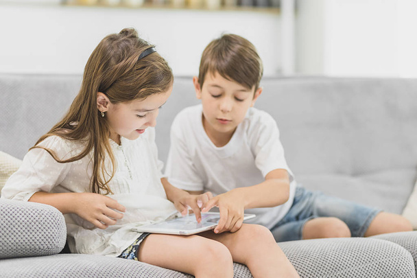 Glückliche Kinder zu Hause auf dem Sofa beim gemeinsamen Spielen mit dem PC-Tablet - Foto, Bild