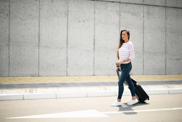 Woman holding coffee and luggage while walking on the street. - Photo, Image