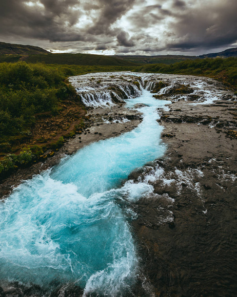 malerischer Blick auf die isländische Natur mit schnellem Fluss und grünen Pflanzen unter bewölktem Himmel - Foto, Bild