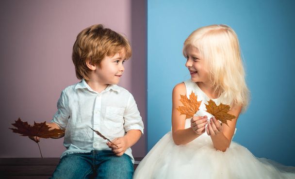 Cute little boy and girl holding leaf on color background. Funny face and happy baby. Children advertise your product and services. Autumn discounts on baby clothes. - Foto, Imagen