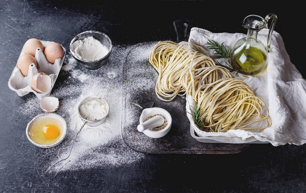 Raw uncooked black pepper spaghetti pasta with flour, egg rosemary, salt and spices and olive oil on vintage metal tray over dark background. Space for text - Foto, Imagen