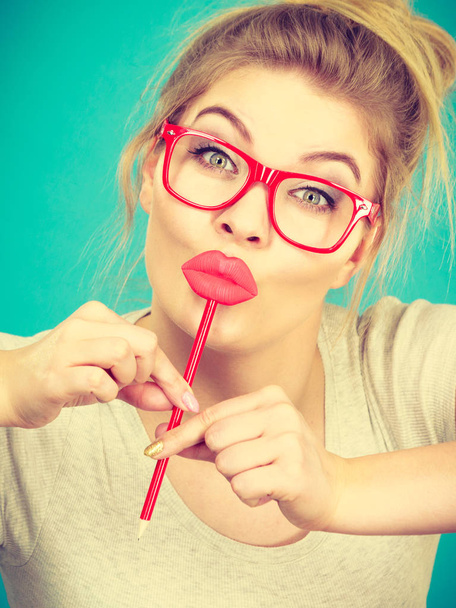Lovely sweet woman casual style nerdy glasses holding red fake lips on stick having fun, on green blue. Photo take and carnival funny accessories concept. - Фото, изображение