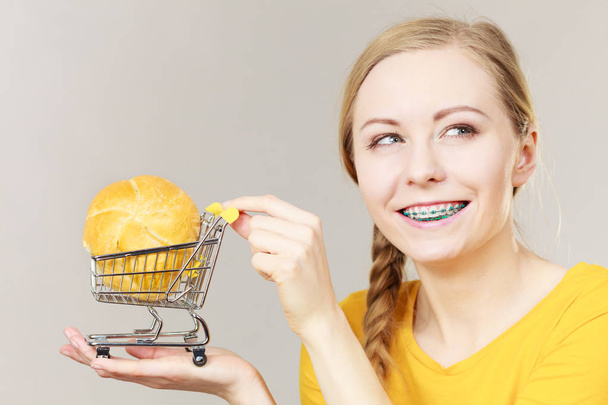 Buying gluten food products concept. Woman holding shopping cart trolley with small piece of bread bun - Фото, изображение
