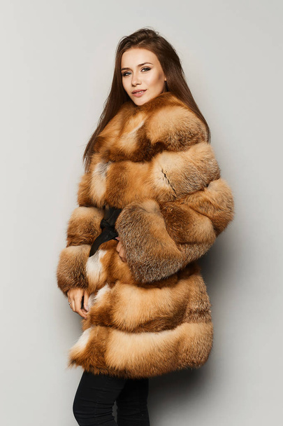 Fashionable and stylish brunette model girl with perfect makeup and blue-grey eyes, in half-length fur coat ginger colour, smiling and posing at studio, isolated. - Foto, Bild