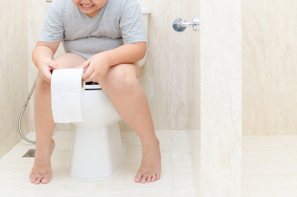 Enfant assis dans les toilettes et tenant rouleau de tissu, constipation diarrhée. concept de santé et propreté
 - Photo, image