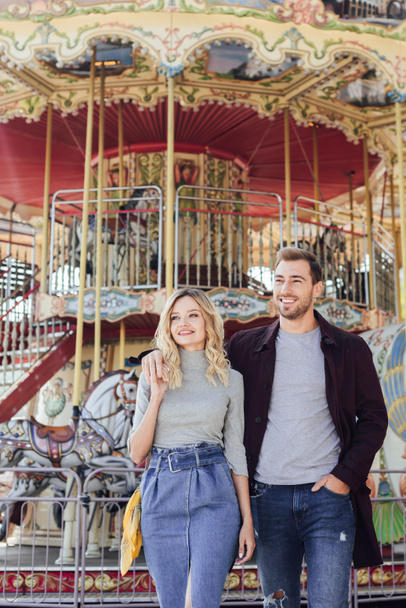 affectionate couple in autumn outfit hugging near carousel in amusement park - Photo, Image