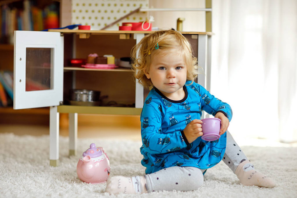 Urocza dziewczynka cute maluch bawiąc się z zabawką kuchnia Happy zdrowe dziecko zabawy z gry role, gry z czajniczek naczynia w domu lub przedszkola. Aktywna córka z zabawką. - Zdjęcie, obraz