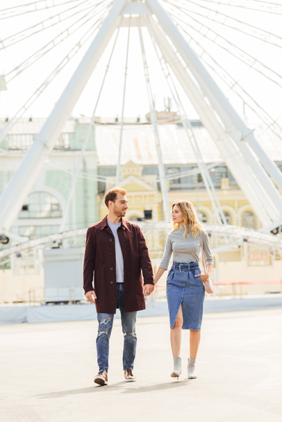couple in autumn outfit holding hands and walking near observation wheel - Photo, Image
