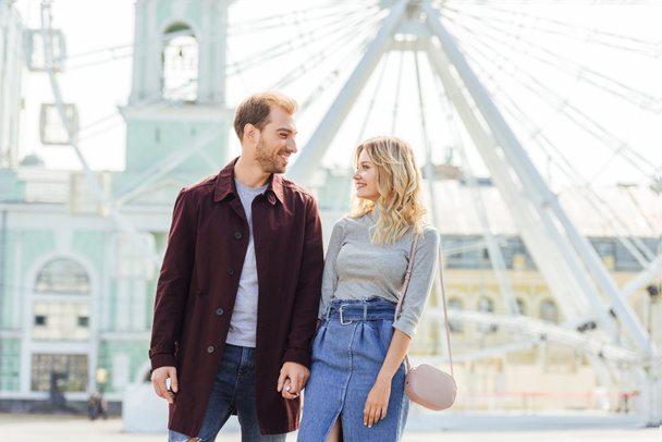 couple in autumn outfit holding hands and looking at each other near observation wheel - Фото, зображення