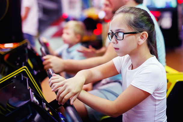 Family mother, father, teen girl with glasses and little boy driving car arcade in game machine at an amusement park. Selective focus. - Photo, Image
