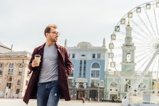 handsome man in autumn outfit walking with disposable coffee cup near observation wheel - Foto, Imagen