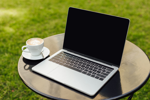 portátil con pantalla en blanco y taza de café en la mesa en el jardín
 - Foto, imagen
