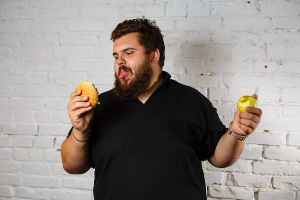 muotokuva mies on hämmentynyt valita mitä syödä välillä terveellisiä tuoreita hedelmiä tai epäterveellistä roskaruokaa
 - Valokuva, kuva