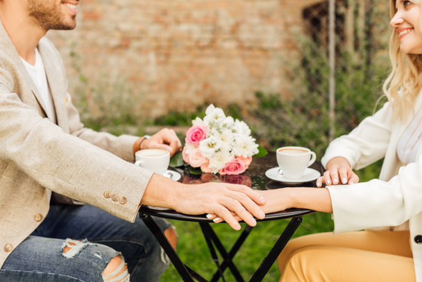 cropped image of couple in autumn outfit holding hands at table in cafe - Photo, Image