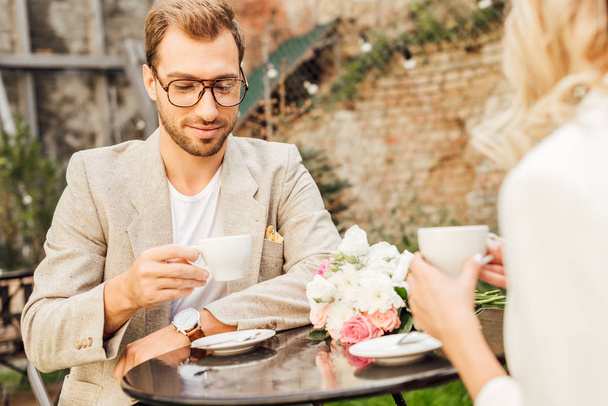 περικομμένη εικόνα του ζεύγους στο φθινόπωρο στολή που κάθεται στο τραπέζι στην καφετέρια - Φωτογραφία, εικόνα