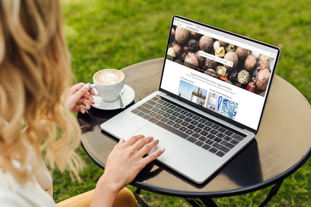 cropped image of woman using laptop with loaded depositphotos page on table in garden - Фото, изображение