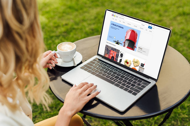 cropped image of woman using laptop with loaded ebay page on table in garden - Foto, imagen