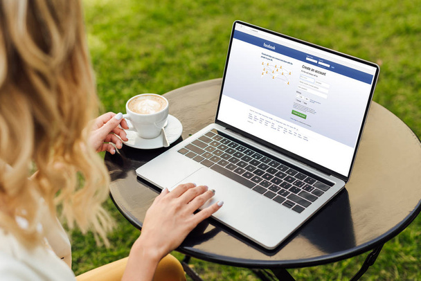 cropped image of woman using laptop with loaded facebook page on table in garden - Foto, Bild
