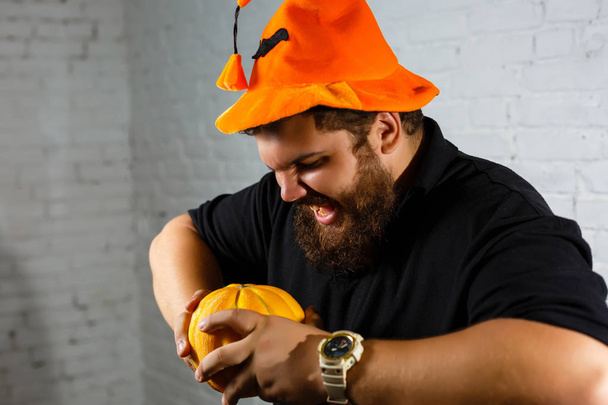 Halloween hipster con barba sorridente con cappello da mago e zucca in mano
  - Foto, immagini