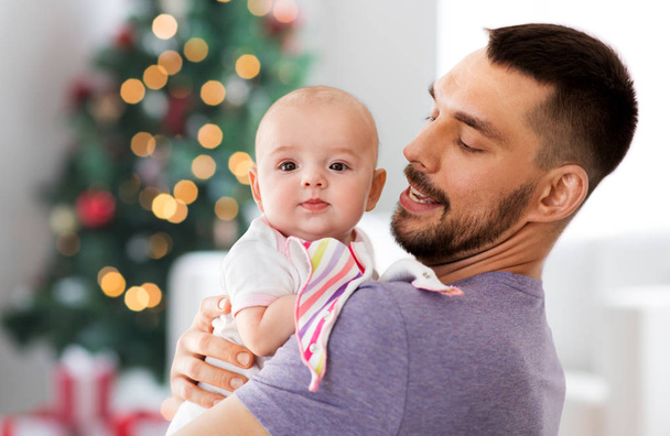 father with baby daughter over christmas tree - Foto, afbeelding