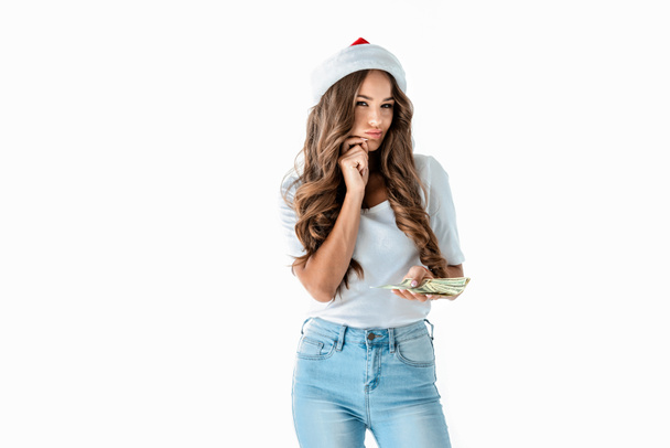привлекательная хитрая девушка в шляпе Санты держит долларовые купюры, изолированные на белом
 - Фото, изображение