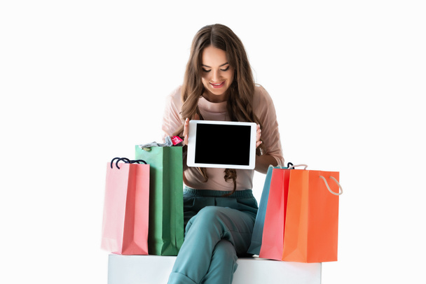 chica sonriente con bolsas de compras mostrando tableta con pantalla en blanco, aislado en blanco
 - Foto, imagen