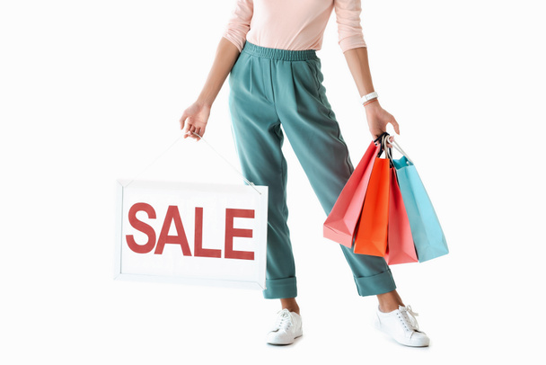 cropped view of beautiful girl holding board with sale sign and shopping bags, isolated on white - Foto, Bild