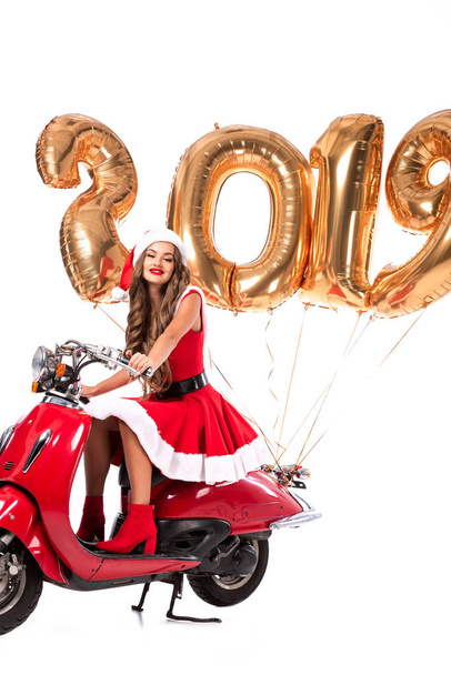 beautiful girl in santa costume driving red scooter with 2019 new year golden balloons, isolated on white - Foto, Bild