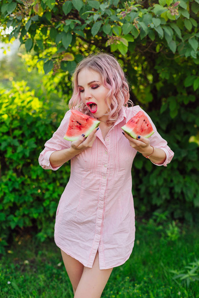 Beautiful young woman with pink hair holding two slices of sweet juicy watermelon - Fotó, kép