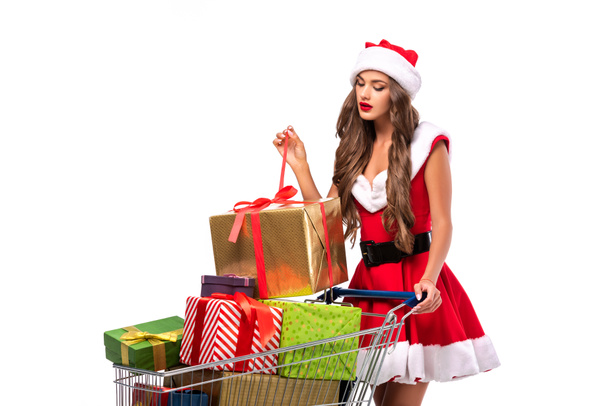 attractive young woman in santa costume with shopping cart full of presents, isolated on white - Foto, afbeelding