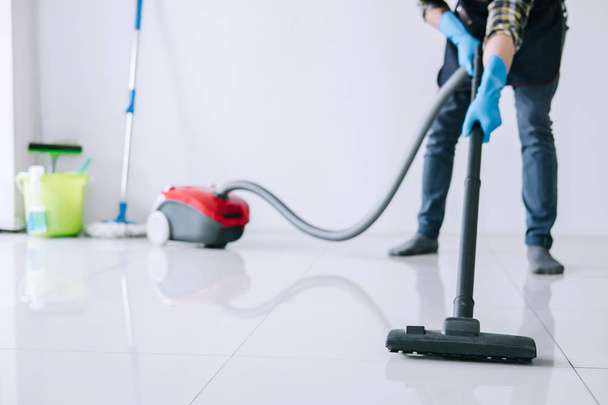 Housekeeping and housework cleaning concept, Happy young man in blue rubber gloves using a vacuum cleaner on floor at home. - Фото, зображення