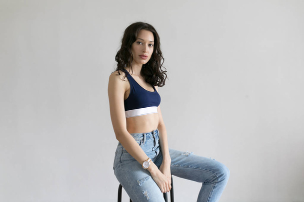 Attractive woman in sports top and jeans poses on white background. - Zdjęcie, obraz