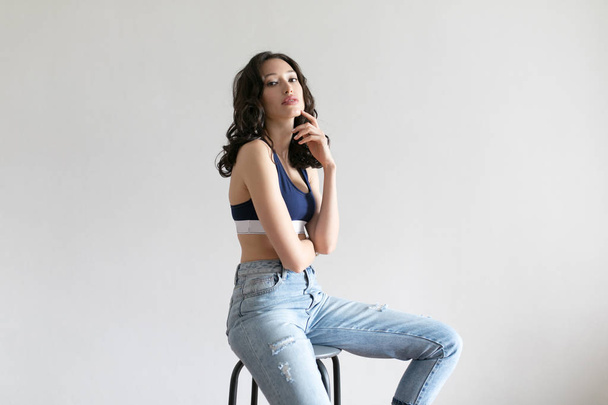 Attractive woman in sports top and jeans poses on white background. - Фото, зображення