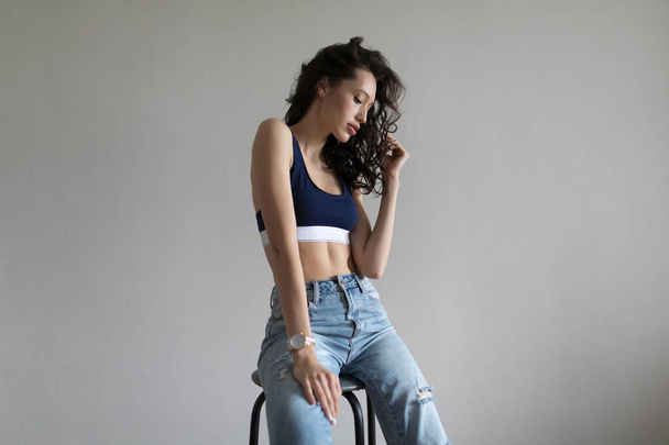 Attractive woman in sports top and jeans poses on white background. - 写真・画像