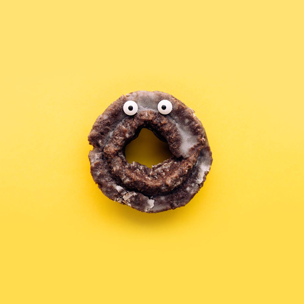 Zabawny szok twarz oszklone ciasto czekoladowe pączki na żółtym tle pastel, minimalne koncepcja Halloween - Zdjęcie, obraz