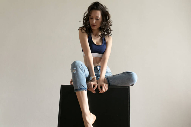 Attractive woman in sports top and jeans poses on white background. - 写真・画像