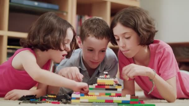Tres niños jugando con ladrillos lego en casa
 - Imágenes, Vídeo