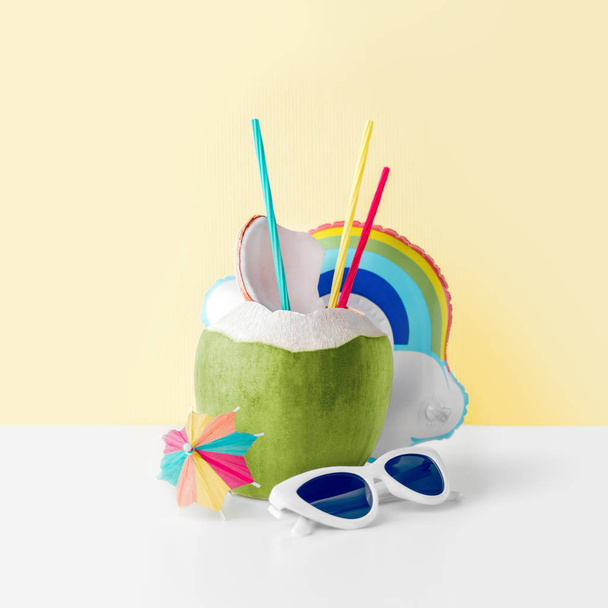 Свіжий кокос на пастельно-жовтому тлі з надувним тримачем для надувних напоїв у веселій хмарі та сонцезахисними окулярами, концепція літнього вітру
 - Фото, зображення