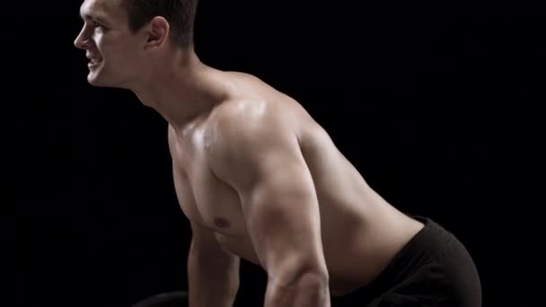 Man is doing exercises with a barbell, training on a black background in the studio - Video