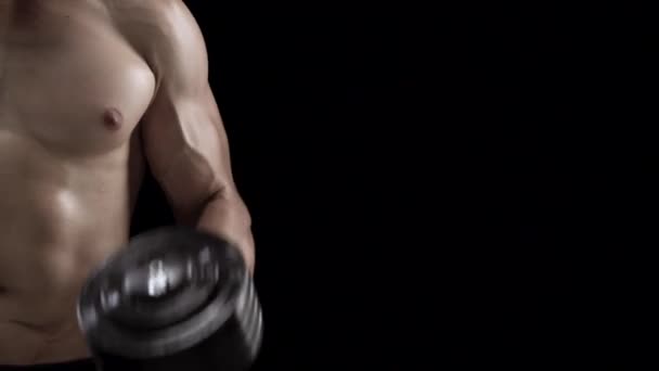Man flexes his hands with dumbbells, training his biceps on a black background in the studio. Half body in the frame - Footage, Video