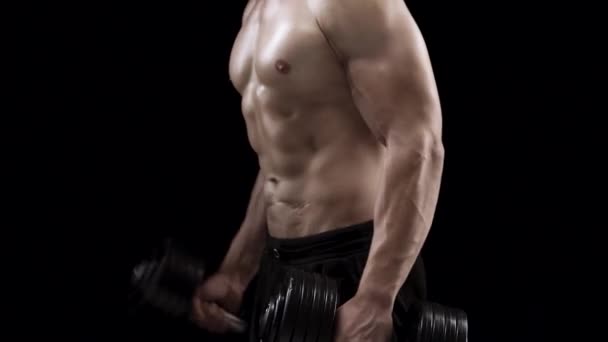 Homem flexiona as mãos com halteres, treinando seus bíceps em um fundo preto no estúdio, vista lateral. Corpo forte muscular
 - Filmagem, Vídeo