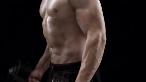 El hombre flexiona sus manos con mancuernas, entrenando sus bíceps sobre un fondo negro en el estudio, vista lateral
 - Metraje, vídeo
