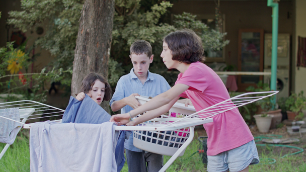 Three kids taking off laundry from the hanging line to the basket - Filmmaterial, Video