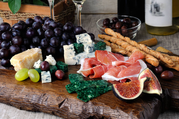Platos para un aperitivo Antipasto en una tabla de madera con jamón, diferentes tipos de queso, uvas e higos en una mesa con vino
 - Foto, imagen