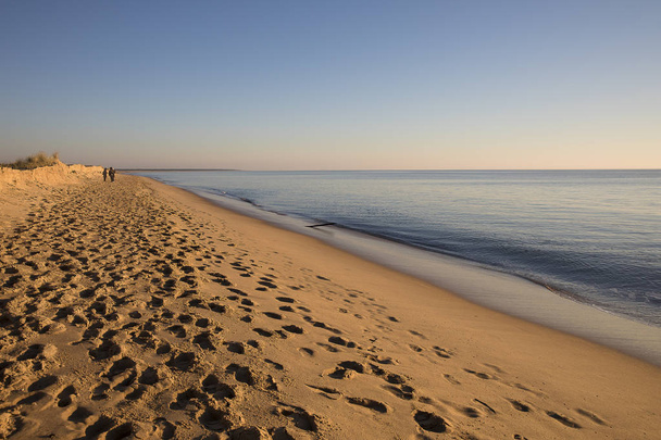 vista sobre uma praia ao pôr do sol com areia dourada um mar tranquilo
 - Foto, Imagem