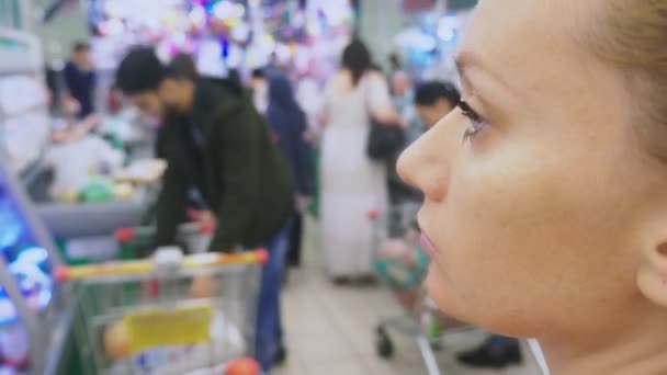 Πορτραίτο μιας νεαρής γυναίκας βαρεθεί σε ένα σούπερ μάρκετ, ανάμεσα σε περνώντας τους πελάτες. 4 k. θόλωμα - Πλάνα, βίντεο