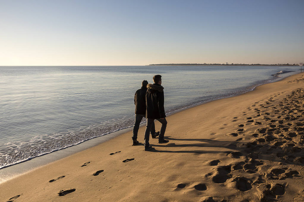 άτομα που περπατούν στην παραλία με ρομαντικό χειμερινό ηλιοβασίλεμα - Φωτογραφία, εικόνα