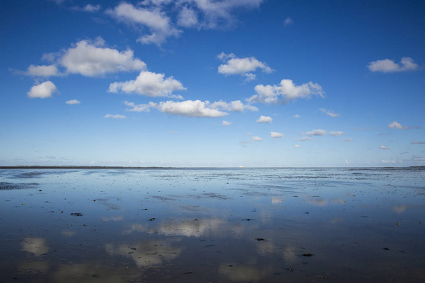 Paisagem marítima com reflexo de nuvens em águas de maré baixa, Waddenzee, Frísia, Países Baixos
 - Foto, Imagem